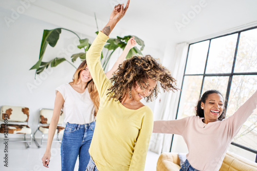 Three funny female friends dancing living room indoors. Multiracial happy women play and celebrate the joy of life Cheerful girls enjoy together at home having fun. 