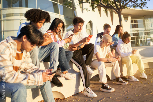 Group of young technology addicts using mobile smartphone outdoor. Multi ethnic millennial generation no social with new trends social media apps. Lens flare photo