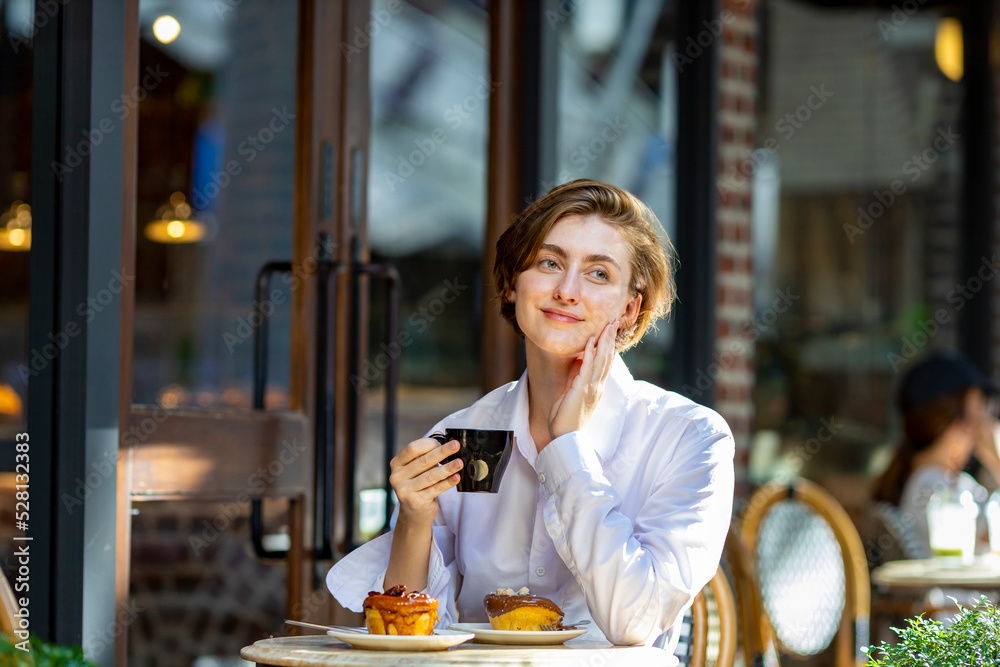 Caucasian woman sipping a hot espresso coffee while sitting outside the european style cafe bistro enjoying slow life with morning vibe at the city square with sweet pastry