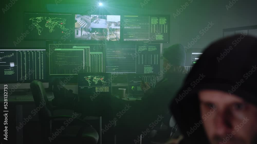 Criminal team Hacker using computer for organizing massive data breach attack on government and big company servers. Dark room surrounded computers