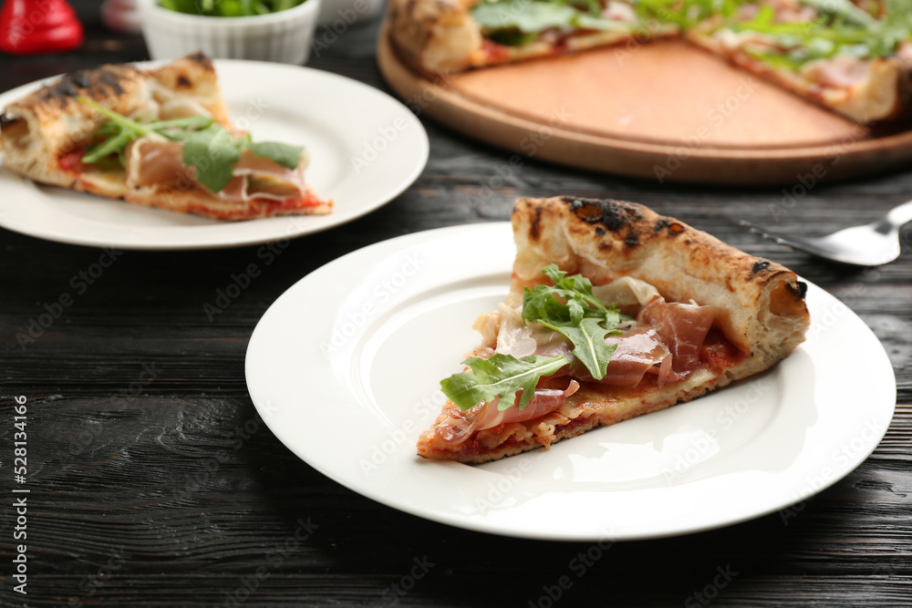 Slice of tasty pizza with meat and arugula on black wooden table, closeup
