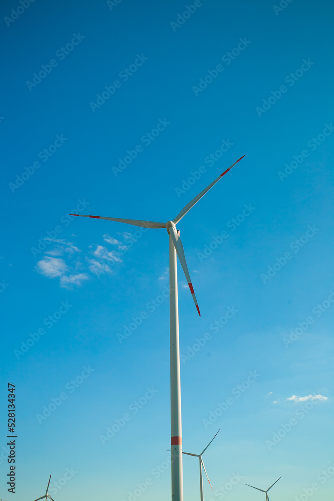 Wind generator on a blue sky background.Alternative natural energy source. Wind energy price.Green renewable energy cost.Windmill renewable energy. Wind generator on a blue sky background.Alternative natural energy source. Wind energy price.Green renewable energy cost.Windmill renewable energy.