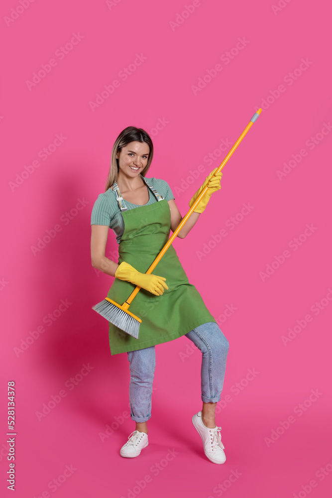 Young woman with yellow broom on pink background Young woman with yellow broom on pink background