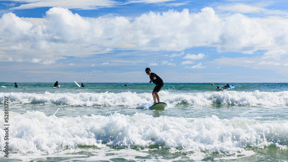 Young boy first success and stands on a soft board while practicing surfing in a beginner's class. Teenager actively balancing on water sports equipment and trying new experiences.