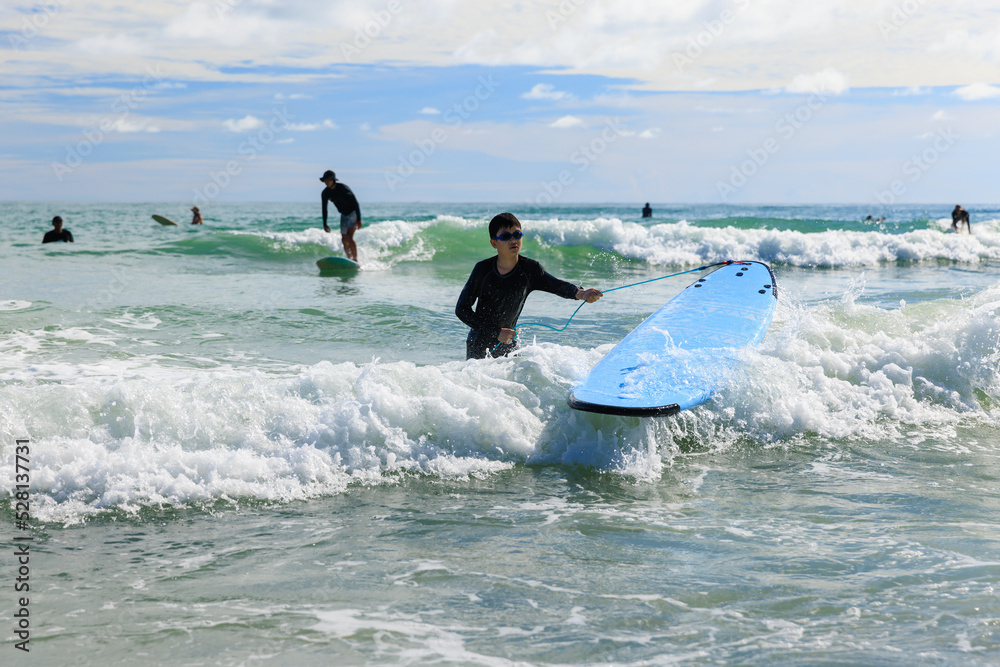 Naklejka premium A young boy eagerly wearing a bathing suit and goggles is practicing surfing.
