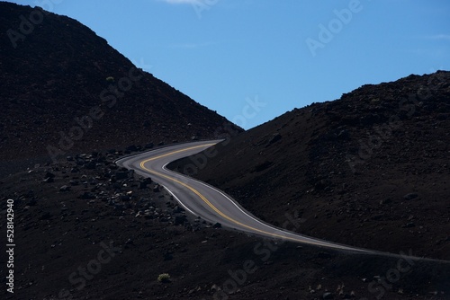 Black road in a blue sky day, going to the top of the hill