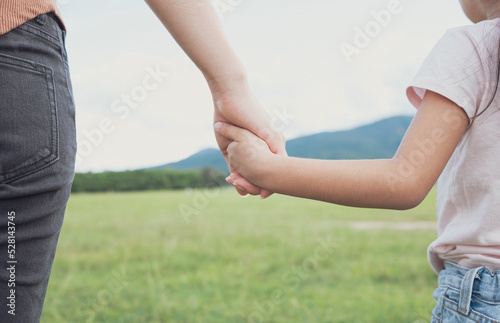 Mother holding hands with his daughter walking in a grass field green nature. Love and healthcare concept