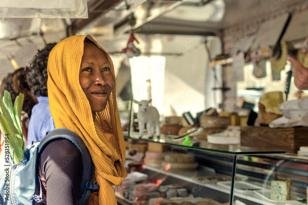 Happy black young Muslim woman in hijab on a market food outdoors, African Islamic lady buying food the street with backpack with vegetables. 