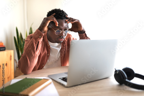 African American black male college student stressed and overwhelmed studying in front of laptop.