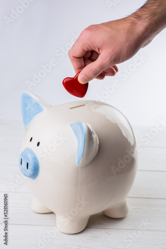 Hand putting red heart coin in piggy bank