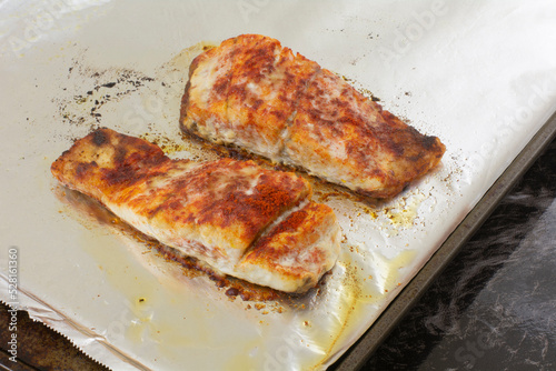 Two baked barramundi fish fillet slices with paprika spice rub on aluminum foil lined baking sheet pan