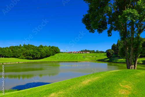 青空のゴルフ場・池越えフェアウェイの最終ホールのコースと丘の上のクラブハウス（千葉県木更津市）