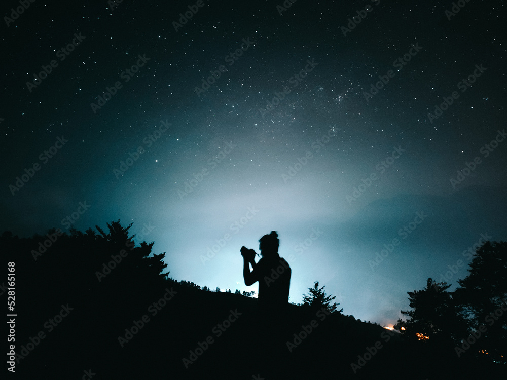 beautiful landscape with silhouette in backlight of man taking pictures in the middle of the night and an incredible starry sky in the background
