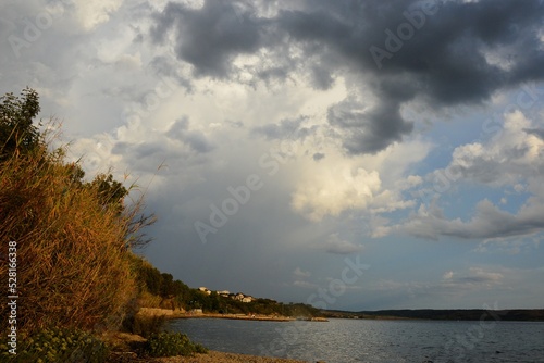 Emerging storm clouds above pebble beach and coastline with settlements in Rtina near Razanac, northern Dalmatia, Croatia.  photo