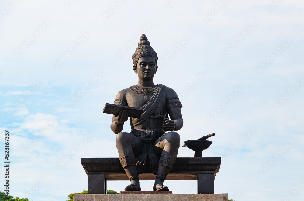 Fototapeta premium King Ramkhamhaeng Monument in Sukhothai Historical Park, Thailand. Ancient Thai king statue holding scripture with traditional attire under blue sky, famous cultural landmark 