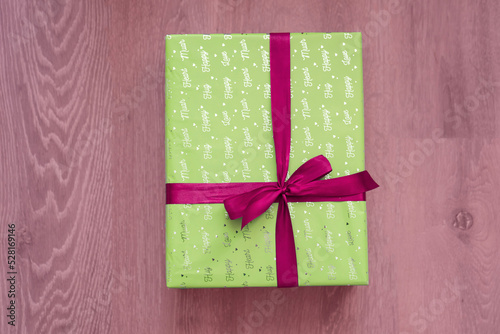 top view of green color gift box with red ribbon bow on light red background. Concept: holiday, celebration, birthday, New Year, Christmas, Valentines Day, Mothers Day, Thanksgiving