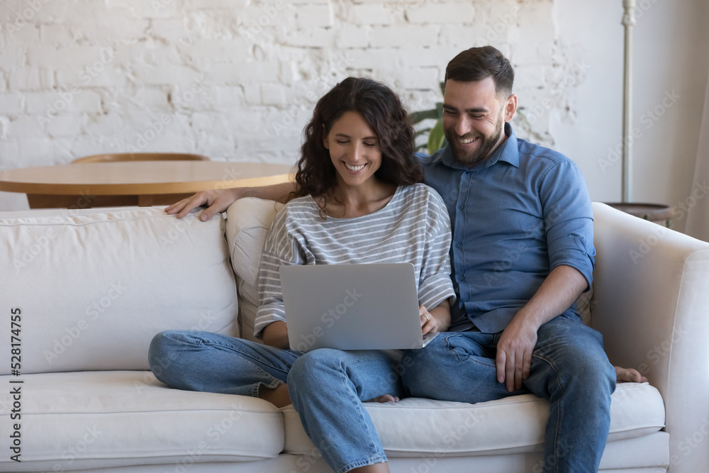 Beautiful millennial couple do e-hopping at home, sit on sofa with laptop smile enjoy distance services for comfort life, make remote order, buy goods feel satisfied. Leisure using modern tech concept Beautiful millennial couple do e-hopping at home, sit on sofa with laptop smile enjoy distance services for comfort life, make remote order, buy goods feel satisfied. Leisure using modern tech concept