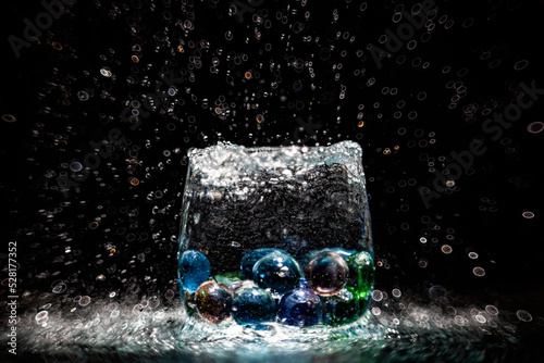 Transparent wine glass with colored glass balls in water splashes with a beautiful blur on a black background