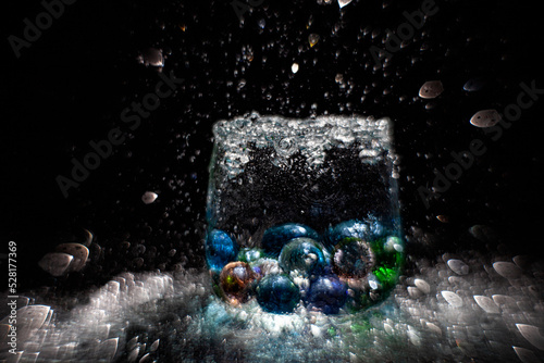 Transparent wine glass with colored glass balls in water splashes with a beautiful blur on a black background