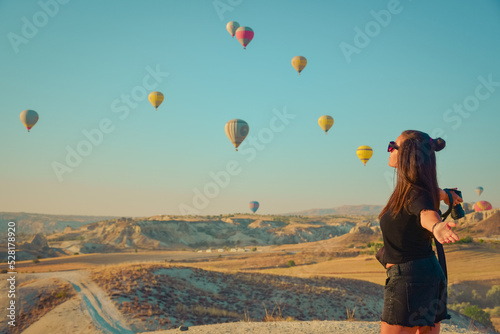 Tourist girl standing and looking to hot air balloons in Cappadocia, Turkey.Happy Travel in Turkey concept Beautiful .Woman taking a photo  on a mountain top enjoying wonderful view 