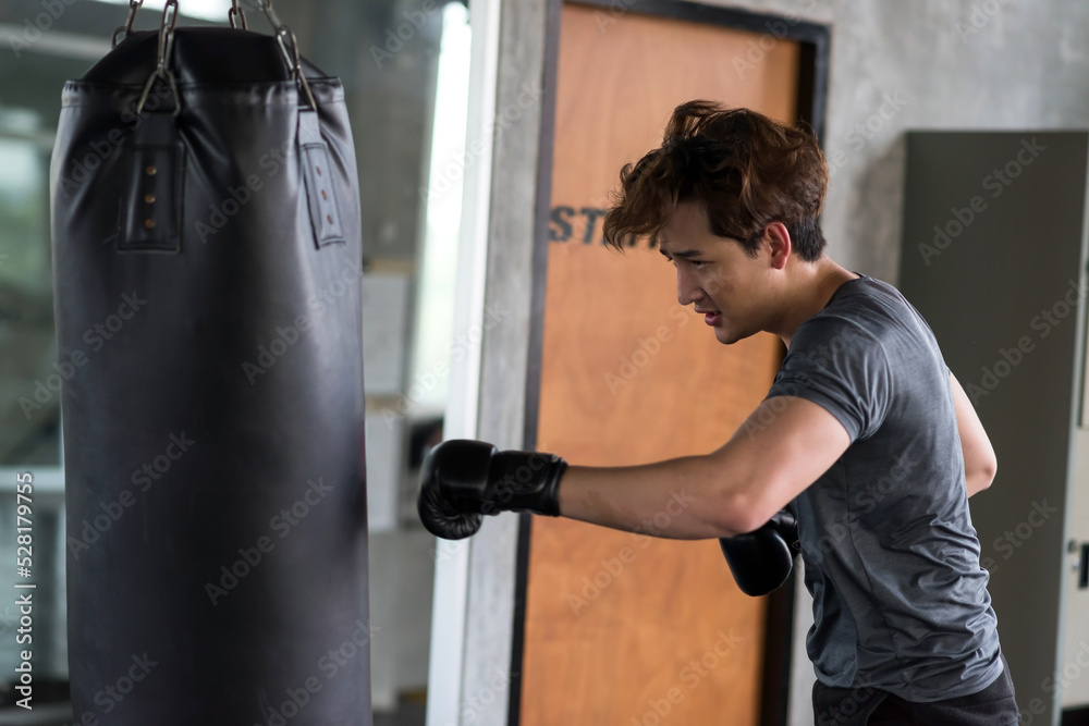 Handsome young boxer punching big bag at fitness gym