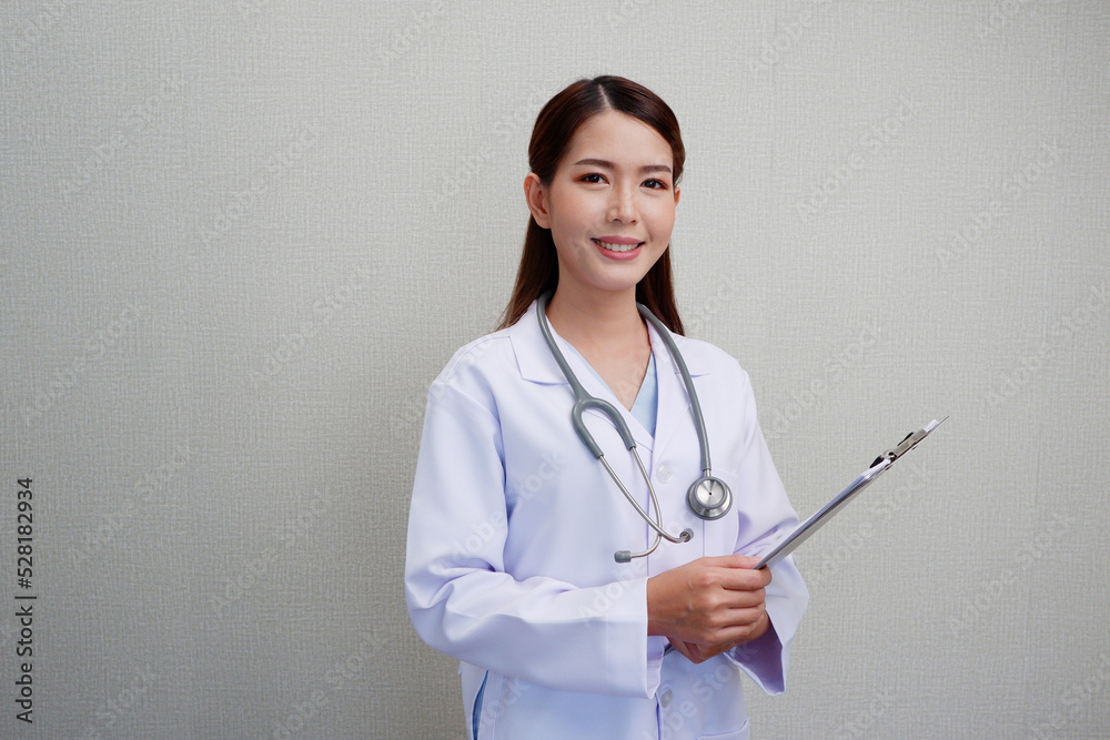 Smiling Asian female doctor puts a stethoscope on her shoulder. wearing a white lab coat standing holding a note board on gray background. Smiling Asian female doctor puts a stethoscope on her shoulder. wearing a white lab coat standing holding a note board on gray background.