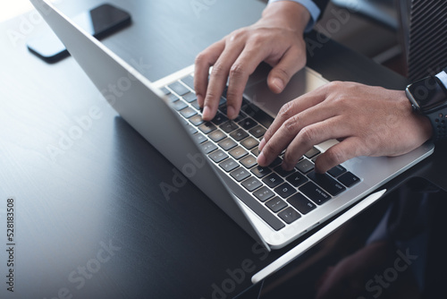Businessman in black suit busy working on new project with notebook computer, digital tablet on table at office. Business man standing at desk, hands typing on notebook computer photo