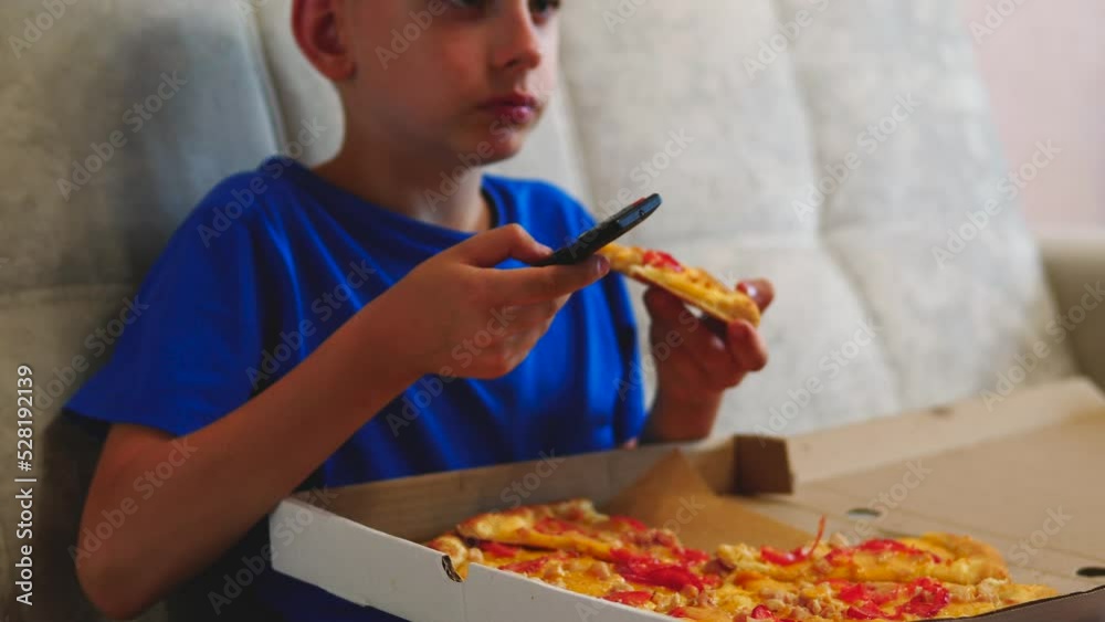 caucasian boy 7-8 years old watching tv eating pizza from a box sitting on the couch at home. child eats pizza. Pizza delivery. the courier brought the food. boy loves fast food