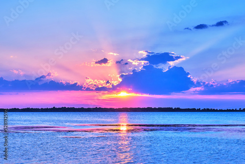 Spectacular sunset in Orbetello, Italy, on the lagoon. The sunrays filtering through the clouds create a dreamy romantic beautiful turquoise pink scenery