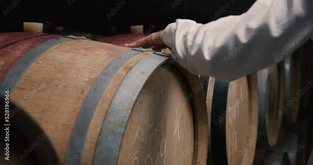 Male owners hand on Wooden oak whiskey, wine, cognac, brandy or beer barrels. A Wine Cellar. Storage Room for Wine in Bottles and Barrels.