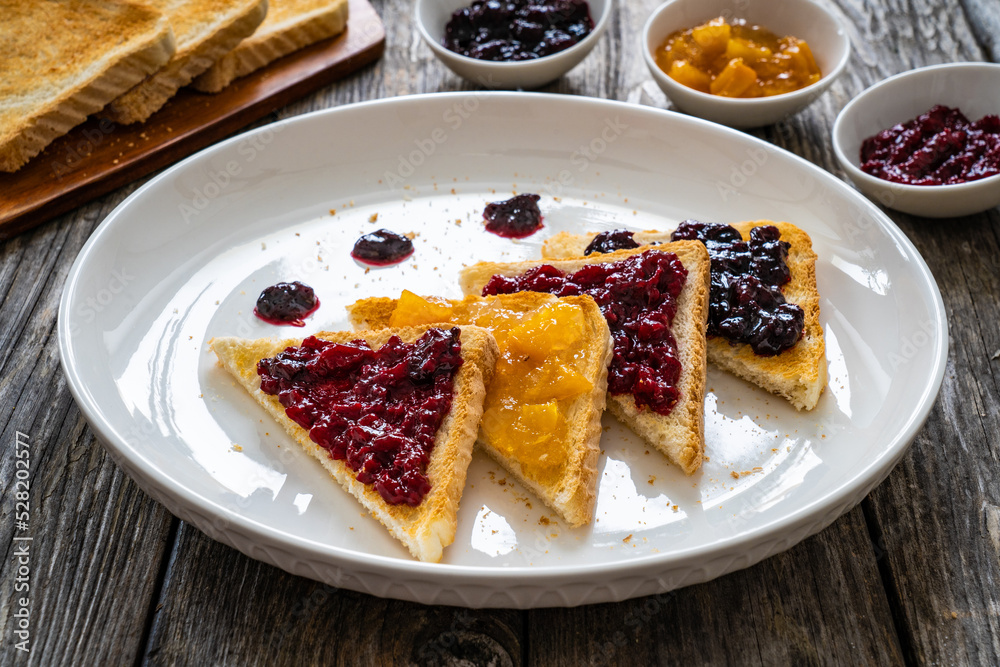 Toasted bread with fruit jam on wooden background
Toasted bread with fruit jam on wooden background