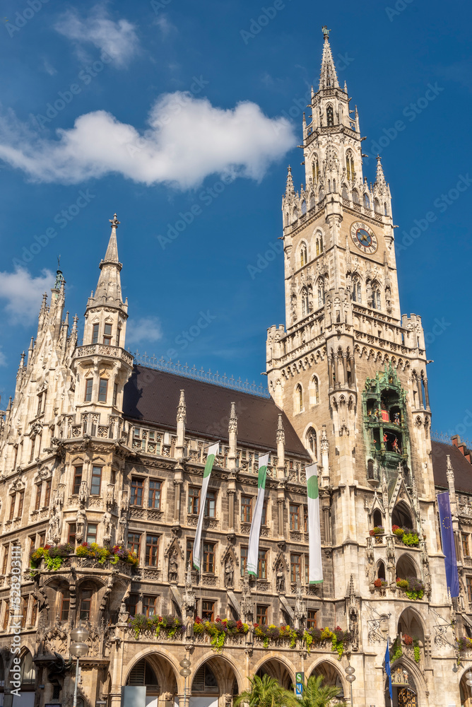 Fototapeta premium Die im Stil der Neugotik gestaltete Fassade des neuen Rathaus mit Rathausturm in der Altstadt von München in Unteransicht vom Marienplatz aus gesehen bei schönem Sommerwetter und blauen Himmel