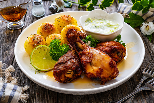 Roasted chicken drumsticks with fried potato and cucumbers in cream on wooden table