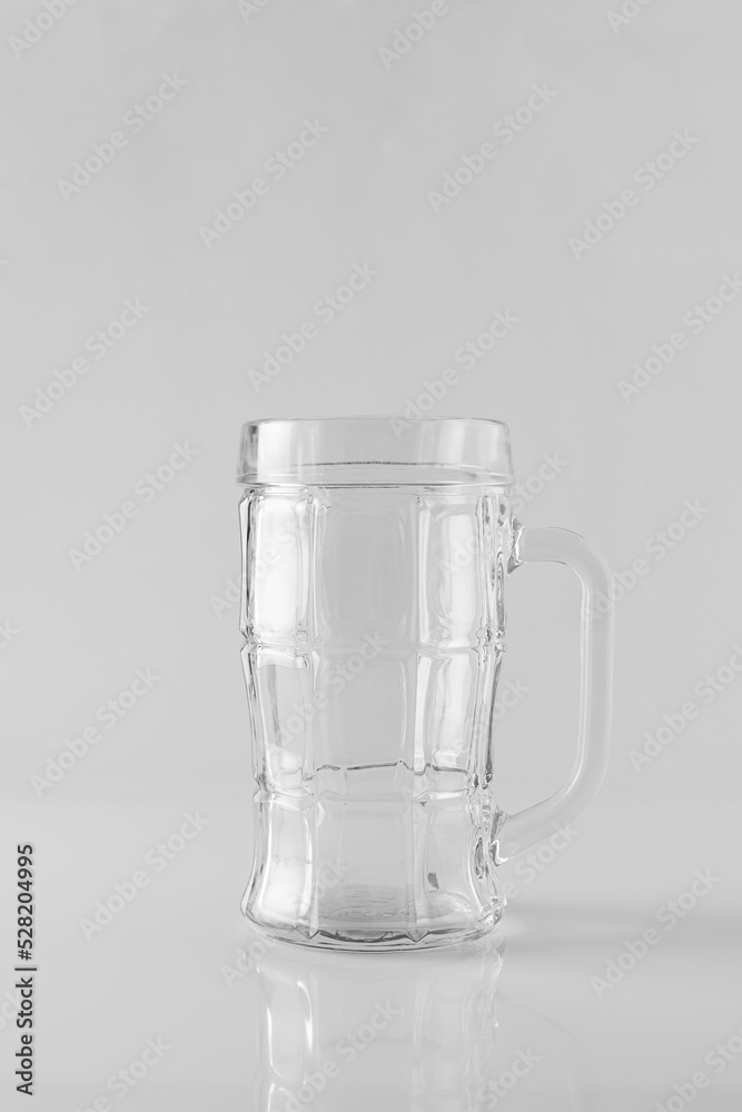 An empty glass beer mug on a white mirrored table. Light background, space for text An empty glass beer mug on a white mirrored table. Light background, space for text