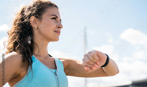 Uses a watch on her hand for training, a sporty woman does fitness exercises on the street.