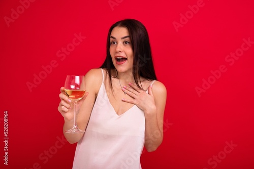 Portrait of a brunette in a white dress with a glass of wine on a red background