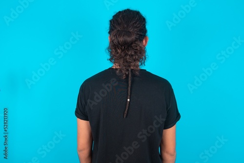 The back view of a young bearded man wearing black T-shirt over blue studio background . Studio Shoot.