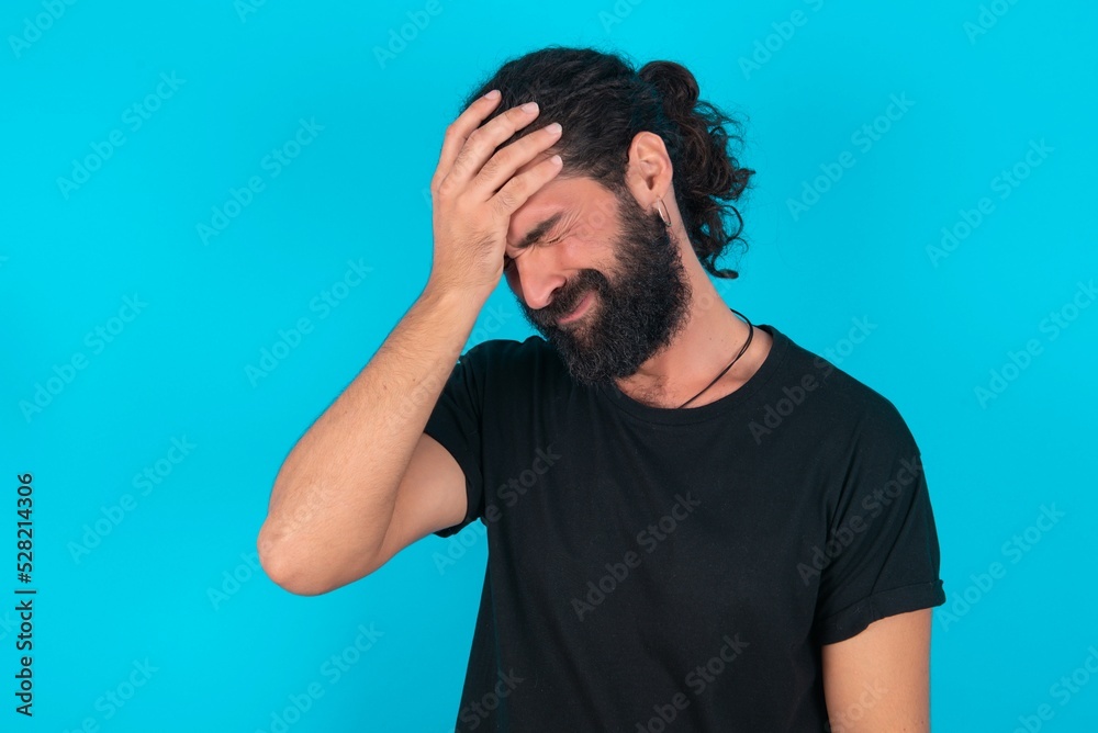A very upset and lonely young bearded man wearing black T-shirt over blue studio background crying, A very upset and lonely young bearded man wearing black T-shirt over blue studio background crying,