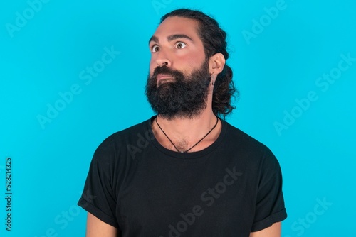 young bearded man wearing black T-shirt over blue studio background making grimace and crazy face, screaming out of control, funny lunatic expressing freedom and wild.