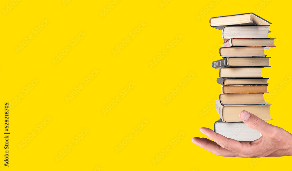 Fototapeta premium Banner with hand holding books stack on yellow background. Knowledge, intellectual development, wisdom, literature power concept. Place for text