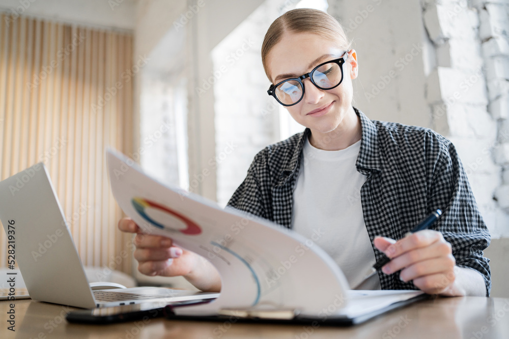 A woman with glasses uses a laptop, works in a new office, uses documents online A woman with glasses uses a laptop, works in a new office, uses documents online