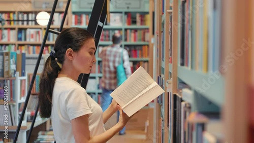 Young woman leafing through a book in library. University. Public library. office bookshelves. Book store 