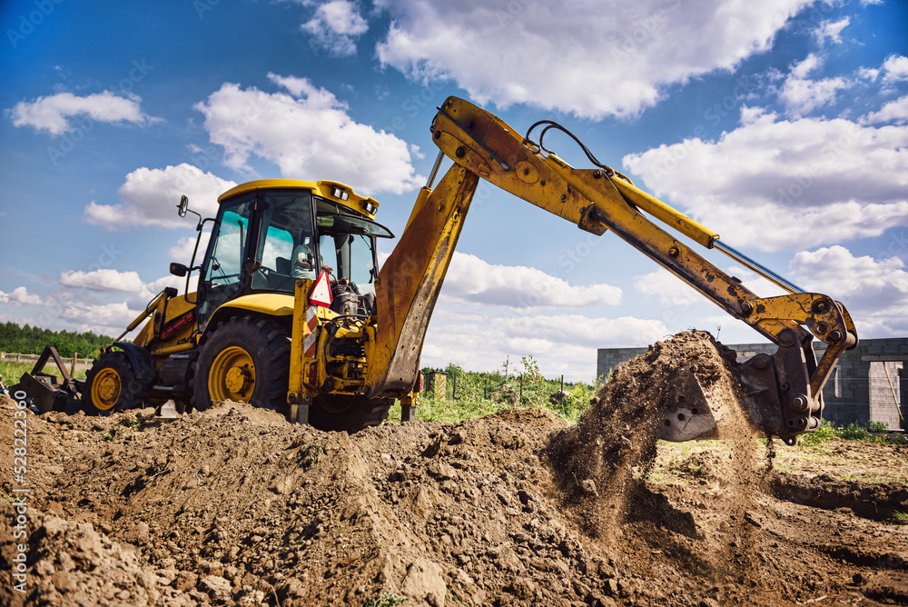 Excavator working at house construction site - digging foundations for modern house. Beginning of house building. Earth moving and foundation preparation.