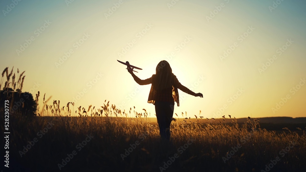 girl kid runs in the park across the field plays with a toy airplane in his hand silhouette at sunset wants an astronaut. funny fantasy children's dream concept. child runs wheat plays with a toy fun