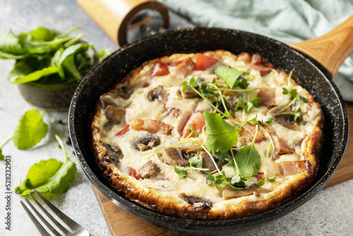 Italian breakfast dish. Rustic omelette (frittata) with mushrooms and bacon on a cast iron pan.