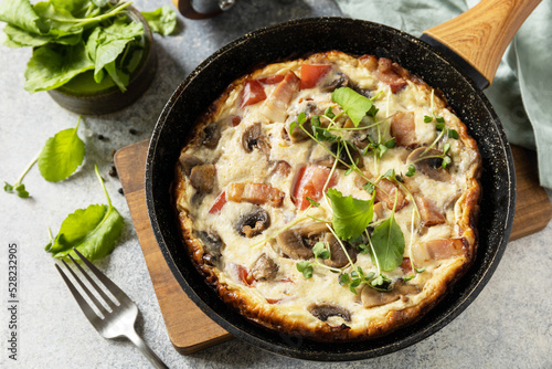 Rustic omelette (frittata) with mushrooms and bacon on a cast iron pan. Italian breakfast dish.