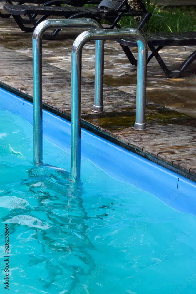 Descent to a bright blue pool with clear water and wooden formwork. Steel railing of the stairs in the pool with blue water. Entrance to the pool Descent to a bright blue pool with clear water and wooden formwork. Steel railing of the stairs in the pool with blue water. Entrance to the pool