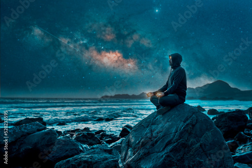 silhouette of a person sitting meditating on the rocks on the coast at night .