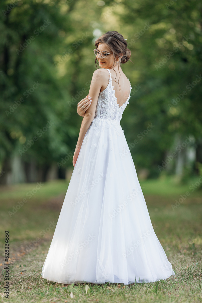 Rearview vertical portrait of young pretty, shiny and charming bride turning back in white wedding dress in natural park