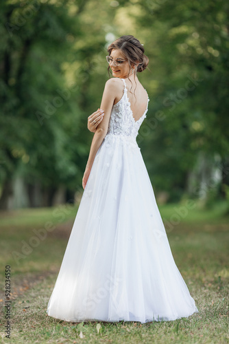 Rearview vertical portrait of young pretty, shiny and charming bride turning back in white wedding dress in natural park